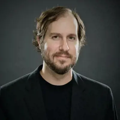 McManus Woodend, white man with brown hair and facial hair wearing a black shirt with black sport coat