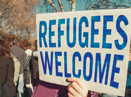Person outside in a crowd holding a sign that reads Refugees Welcome.
