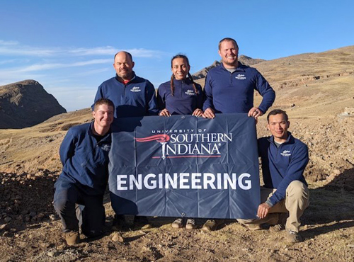 4 men and 1 woman outdoors holding a flag with a USI logo and the word ENGINEERING on it
